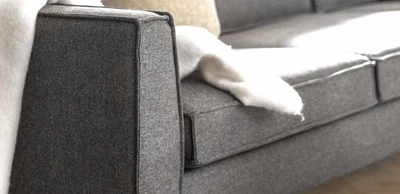 Närbild av mörkgrå soffa med vit pläd liggande över sig