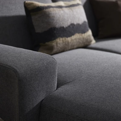 Närbild av mörkgrå soffa med kudde i brungrå nyanser