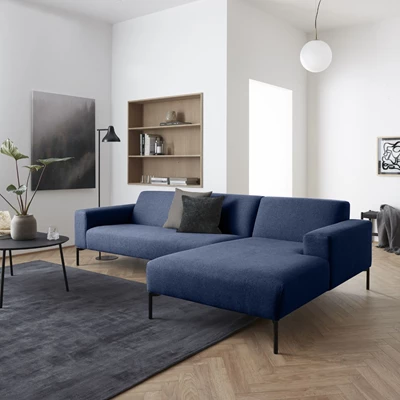 Soffa med schäslong i mörkblå design stående på trägolv med några av benen på svart matta