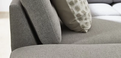 Närbild av soffa i ljusgrå nyans med kudde liggande ovanpå