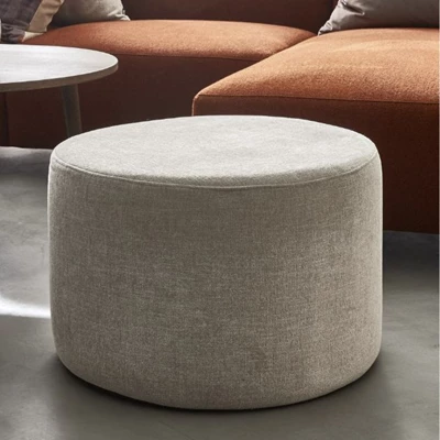 Puff i vit nyans stående framför soffa i rödaktig design