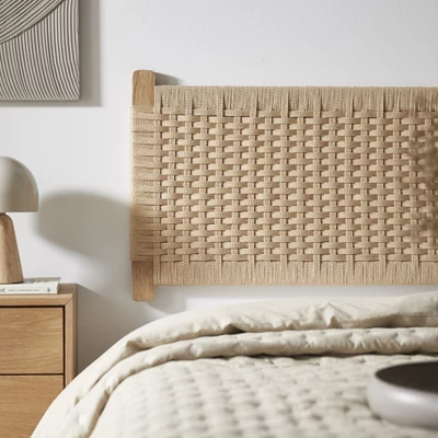 Närbild av säng med överkast och sandfärgad flätad sänggavel