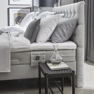 Ställbar säng i grått sedd från sidan med ett sängbord bredvid