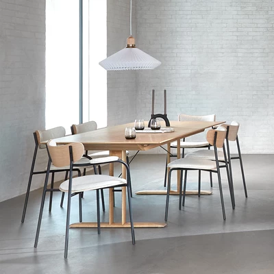 Matbord i ekträ med 6 stycken stolar i ek med stålben och handtag, och med sits i vit bouclé. Med en vit plisserad taklampa. På bordet står en ljusstake, ett fat och tre dricksglas.