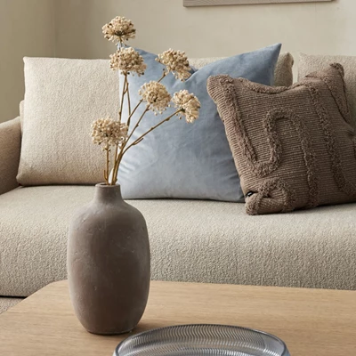 Brunaktig vas med torkade blommor stående på soffbord