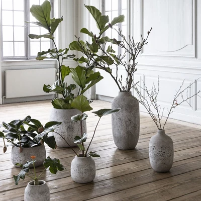 Samling av gråa vaser stående på golvet med olika växter i