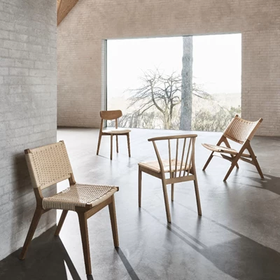 4 stolar i bruna nyanser står i ett grått och minimalistiskt rum med stort fönster