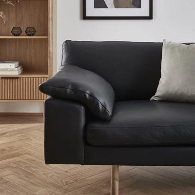 Svart soffa i läder stående på trägolv med vit kudde på en av sittplatserna