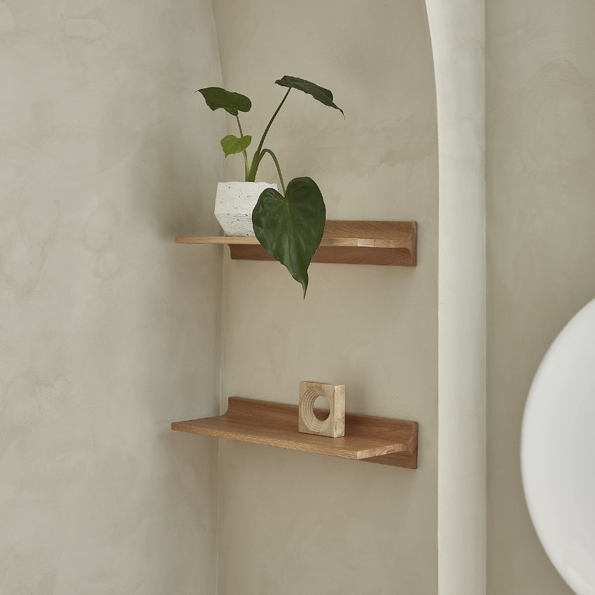 Väggmonterad trähylla med dekorativa föremål och grön växt i ljust rum.