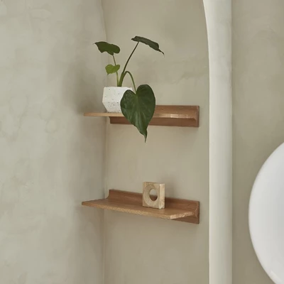 Väggmonterad trähylla med dekorativa föremål och grön växt i ljust rum.