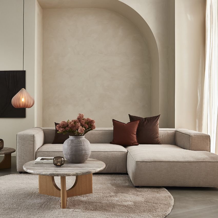 Beige hörnsoffa med dekorativa kuddar och runda bord i elegant rum.