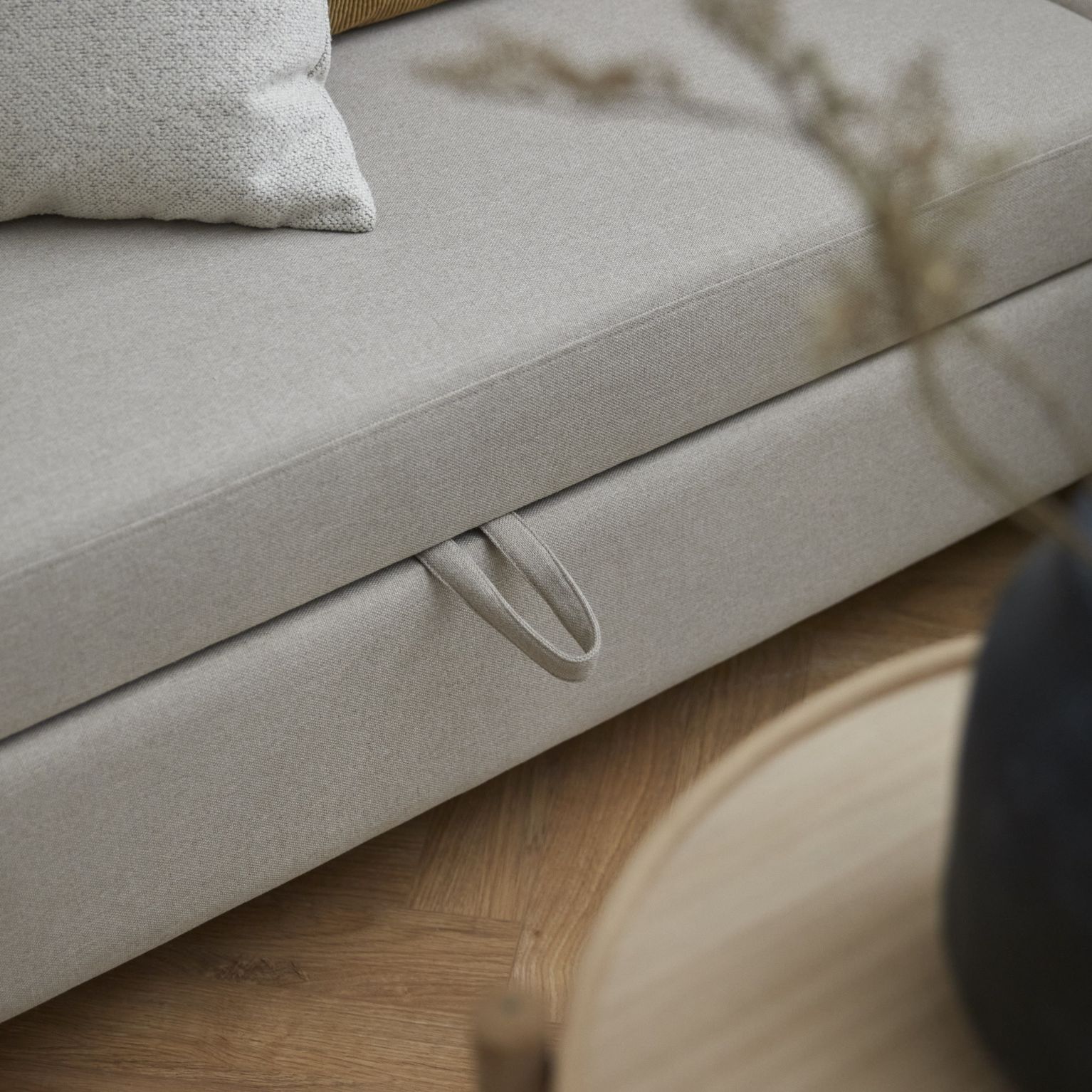 Detalj av en ljusgrå soffa med ett integrerat trähandtag för enkel justering av sittytor, placerad över ett trägolv.