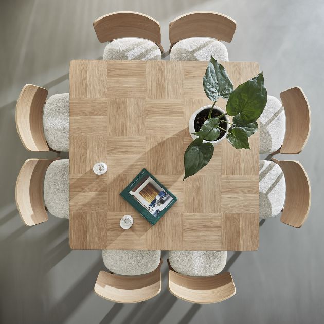 Fyrkantigt träbord sett uppifrån med åtta stolar och växt i mitten.