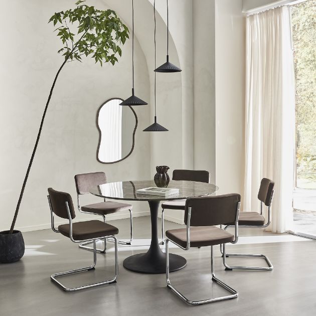 Runt matbord med svarta stolar, hänglampor och stora fönster i ljust matrum.