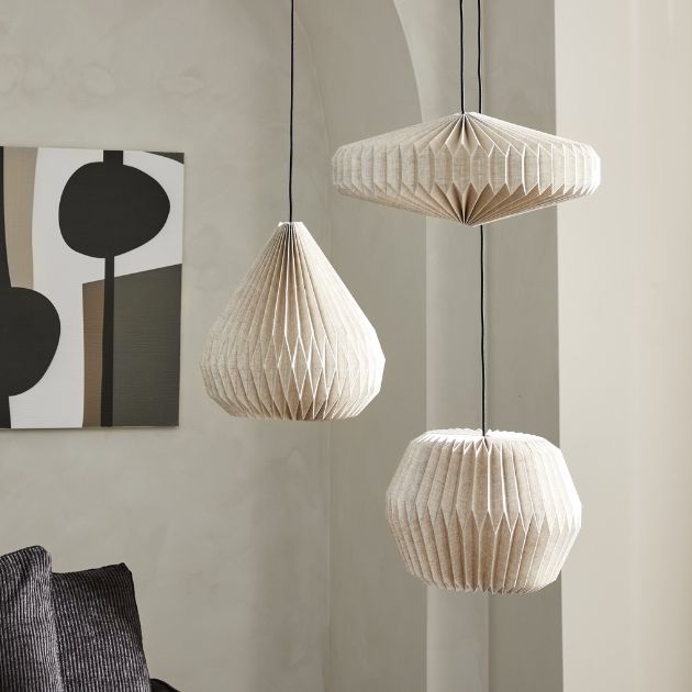 Tre taklampor i tyg med veckad struktur mot ljus vägg och modern konst.