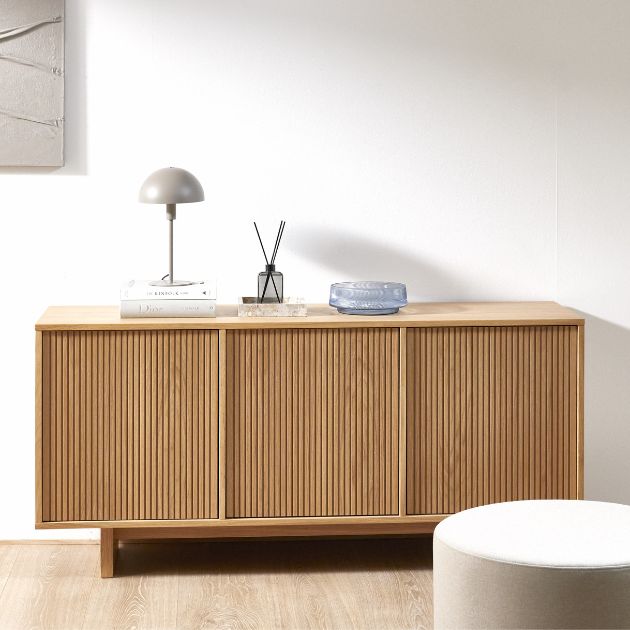 Skänk i ljust trä med bland annat bordslampa, vas och annan dekoration ovanpå