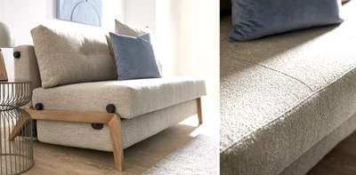Bäddsoffa med träram i grå textil som står på ett trägolv med kuddar på sitsarna