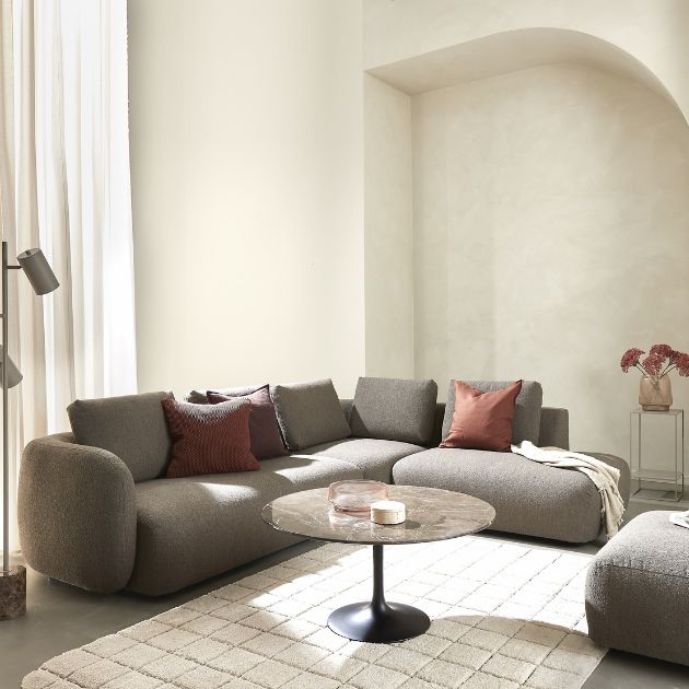 Stilren grå modulsoffa med rundade former, kombinerad med ett marmorbord och rostfärgade kuddar i en ljus interiör