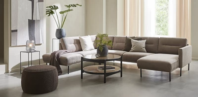 Elegant ljusbeige hörnsoffa med svarta metallbord och gröna växter, placerad i ett rum med välvda väggar och stora fönster.