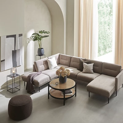 Elegant ljusbeige hörnsoffa med svarta metallbord och gröna växter, placerad i ett rum med välvda väggar och stora fönster.