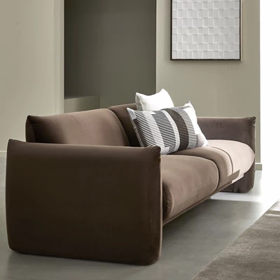 Modern brun soffa med mjuka kuddar i neutrala färger, placerad mot en minimalistisk vägg med geometrisk konst