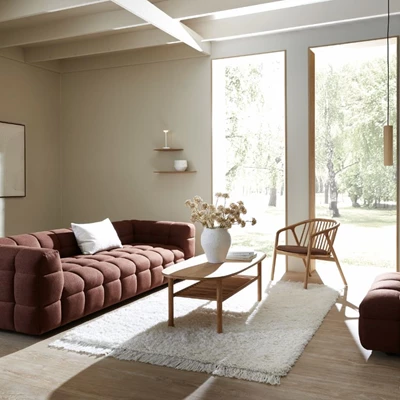 Inblick i ett vardagsrum med en röd soffa med djuphäftning, ett soffbord i trä, en fåtölj i trä och några väggmonterade hyllor i trä