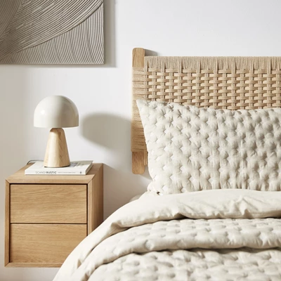 Sänggavel i pappersflätning hängande på väggen tillsammans med en bäddad säng, ett hängande sängbord och en bordslampa