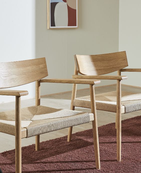 Två ljusa trästolar med flätad sits placerade på en röd matta i ett minimalistiskt matrum