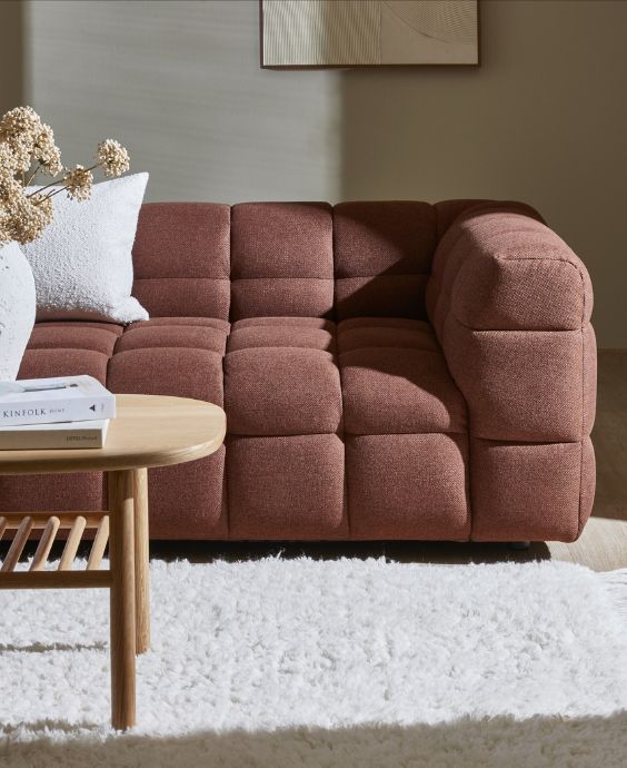 Modern brun soffa med en mjuk, stoppad yta, placerad på en ljus matta vid ett soffbord i trä