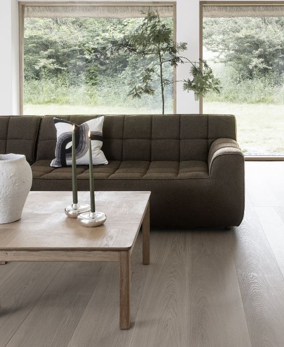 Elegant vardagsrum med en mörkbrun soffa, ett fyrkantigt soffbord i trä och stora fönster som skapar en ljus och luftig atmosfär.