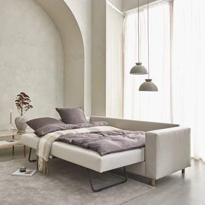Uppfälld bäddsoffa i beige med två taklampor hängande ovanför.