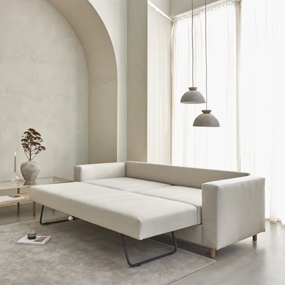 Utfälld bäddsoffa i beige med två taklampor hängande ovanför.