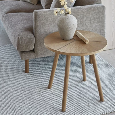 Sidobord i ljust trä stående bredvid en grå soffa