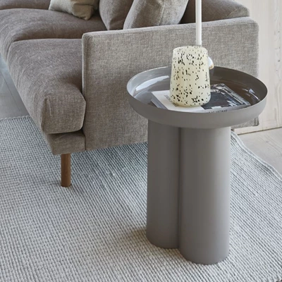 Sidobord med organiska, konstnärliga former stående på en matta vid soffan