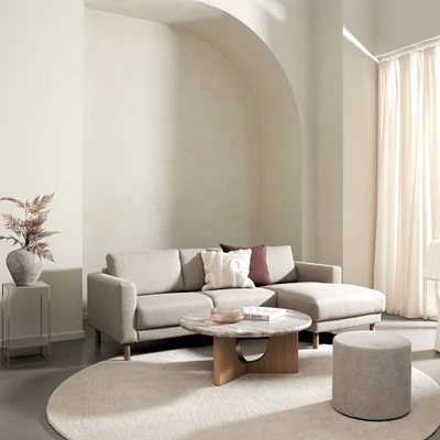Beige schäslongsoffa på en rund matta tillsammans med ett soffbord med travertinbordsskiva
