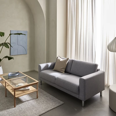 Tvåsitsig grå soffa på betonggolv med ett soffbord i trästomme och glasskiva
