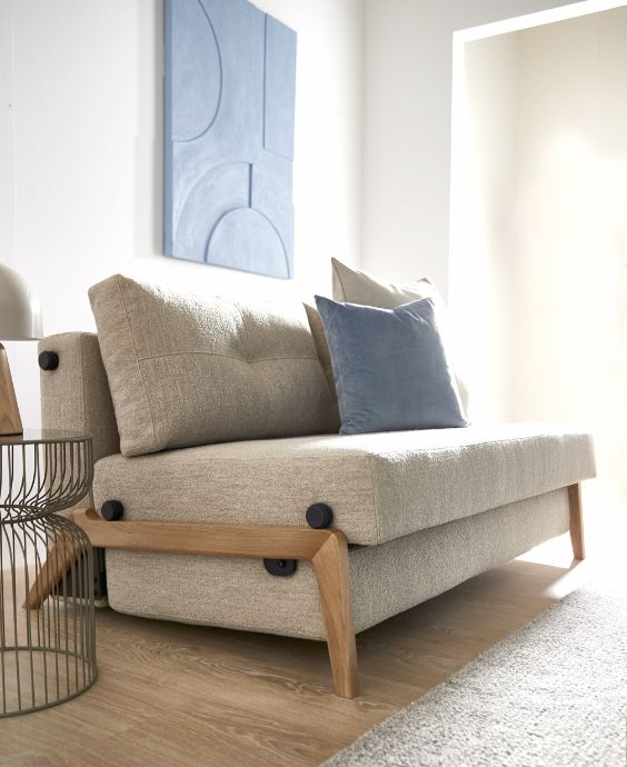 Mysigt vardagsrum med en modern soffa i ljusgrått, utrustad med blåa och gråa kuddar, över ett mjukt matta nära ett fönster med massor av naturligt ljus