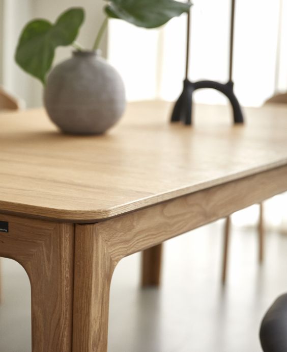 Närbild av kanten på ett elegant träbord som visar detaljerat hantverk och en slät finish, med en dekorativ vas i bakgrunden