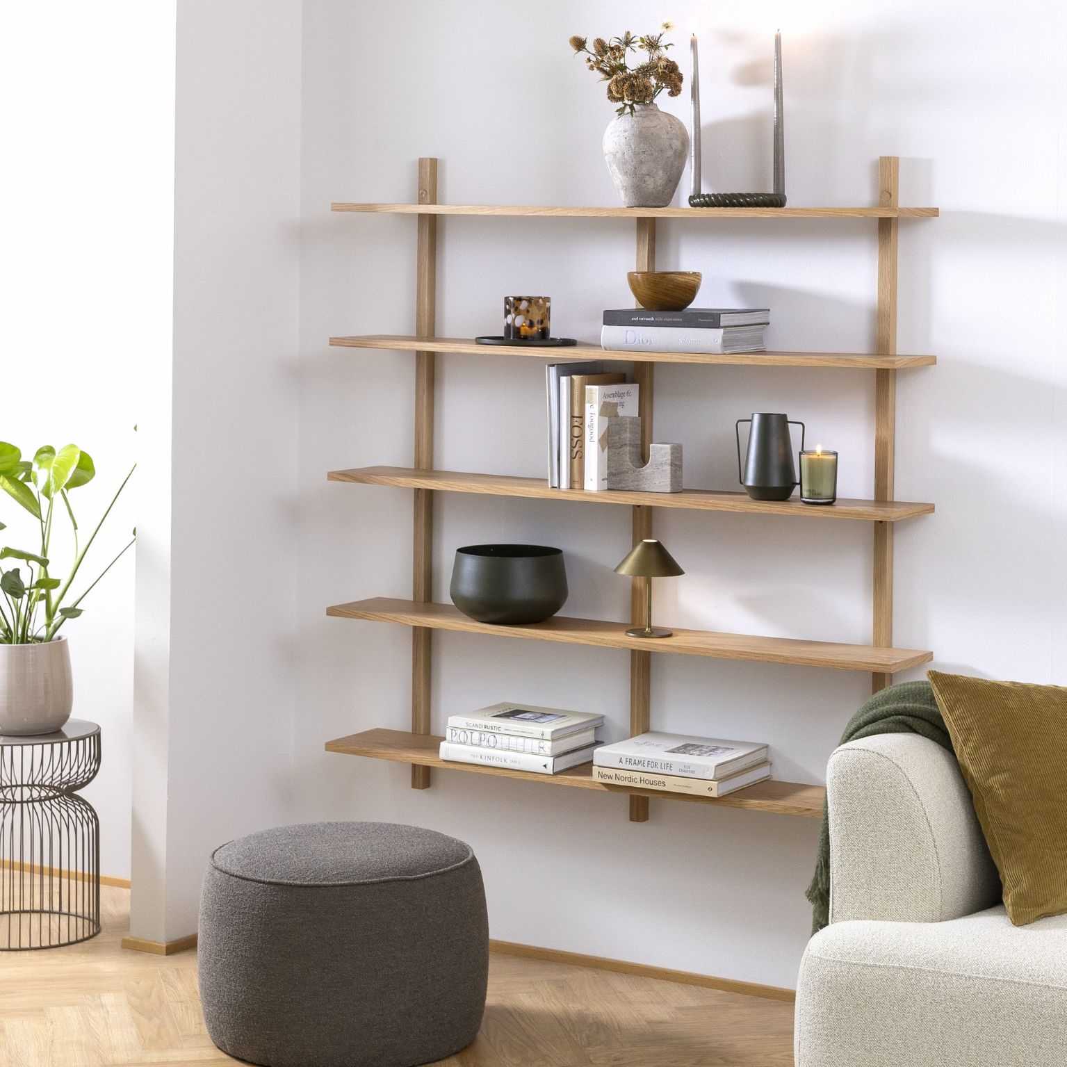 Vägghylla i trä med 5 hyllor, med bland annat böcker, vaser och lampor stående på.