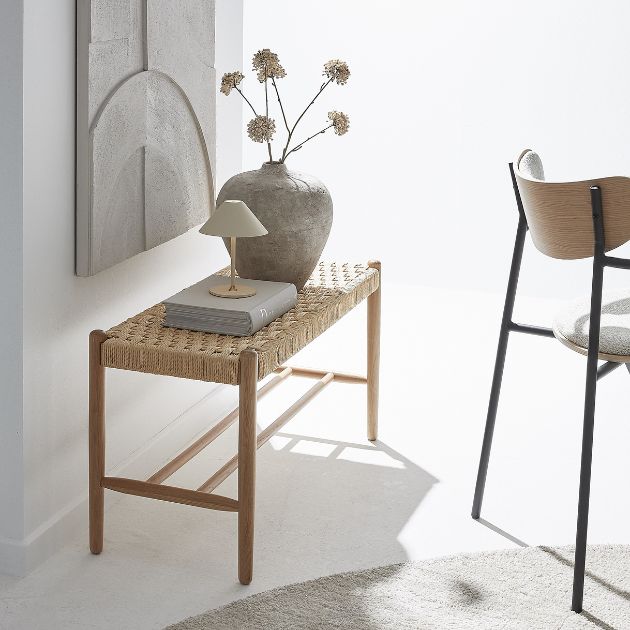 Bänk med flätad sits stående på vit matta med en grå bild hängande ovanför