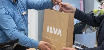 Expedit i blå skjorta som ger en papperspåse med ILVA-logotyp till kund