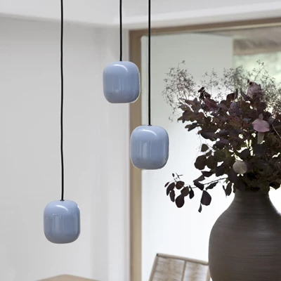 Närbild av tre blå glaspendellampor som hänger över ett matbord, kombinerat med en mörk vas med torkade blommor