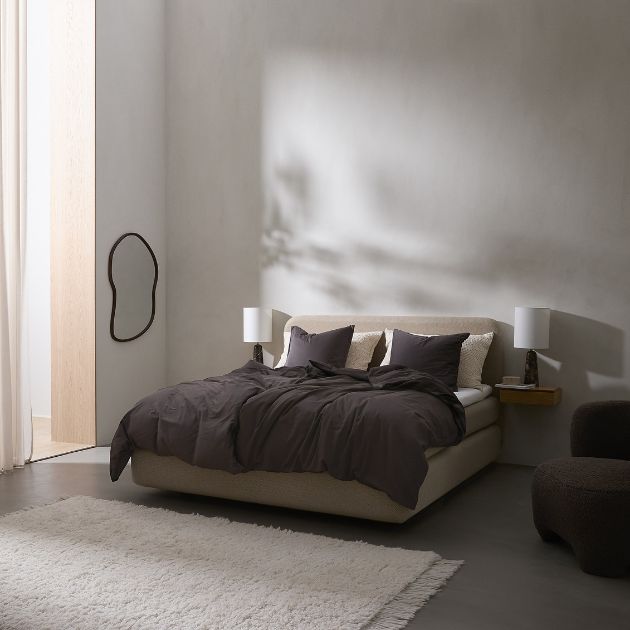 Polstrad dubbelsäng med mörkt sänglinne och minimalistisk inredning