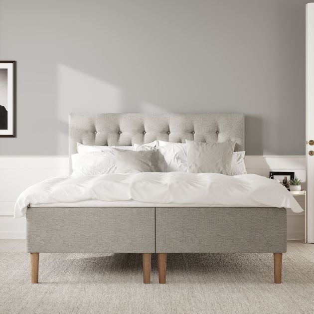 Grå kontinentalsäng med knappdetaljerad gavel och vitt sänglinne