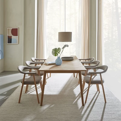 Matbord med 6 matstolar runt om. Det står på en vitaktig matta, och över bordet hänger en taklampa.