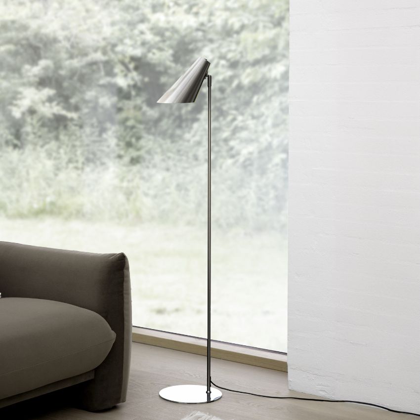 Golvlampa i minimalistisk design i borstat stål, placerad på trägolv bredvid en brun soffa