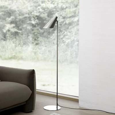 Golvlampa i minimalistisk design i borstat stål, placerad på trägolv bredvid en brun soffa