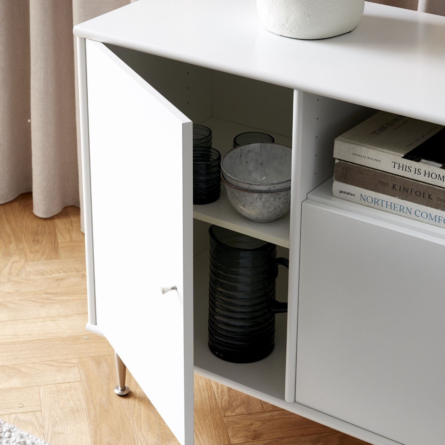 Vit hylla på ben med en öppen dörr som visar innehållet.