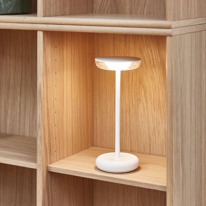 Närbild av en trådlös vit bordslampa som står på en kubikhylla i trä.