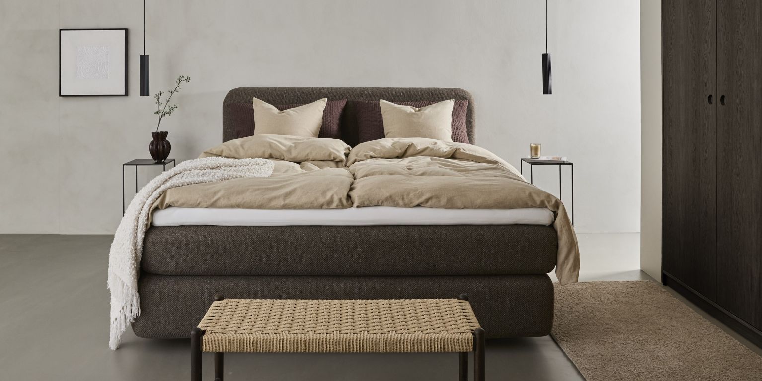 Stilfullt sovrum med stor brun säng, beige överkast och minimalistisk dekor